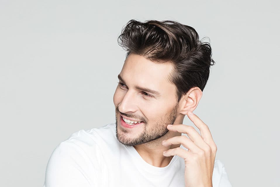 Portrait of handsome young man against grey background. He is looking away and smiling.